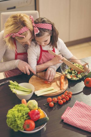 Foto de Madre e hija cortando verduras y haciendo ensalada. Concéntrate en la hija - Imagen libre de derechos