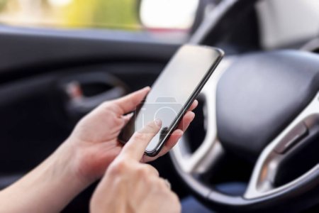 Photo for Detail of female hands holding a smart phone and typing a text message while sitting in a car; park by the side of the road and safely use smart phone; traffic safety concept - Royalty Free Image
