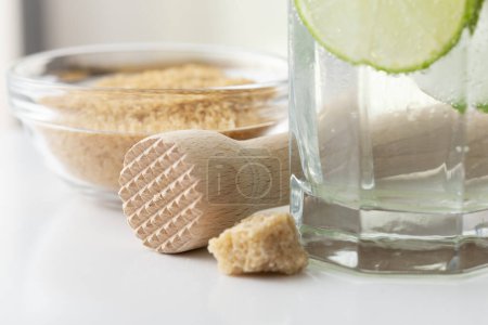Photo for Detail of a brown sugar in a bowl, rustic brown sugar cubes and a glass of cold mojito cocktail with white rum, lemon juice and tonic - Royalty Free Image