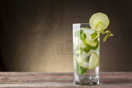 Photo for Mojito cocktail with lots of ice, white rum, lemon juice and tonic, decorated with lime slices and mint leaves on a rustic wooden table - Royalty Free Image