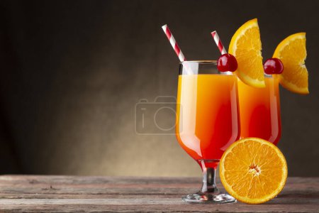 Téléchargez les photos : Deux cocktails froids au lever du soleil à la tequila, jus de grenade et jus d'orange décorés de tranches d'orange et de cerises de marasquin - en image libre de droit