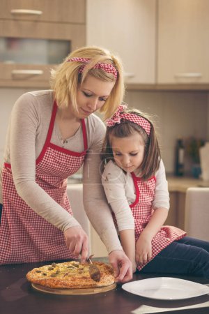 Photo for Mother and daughter cutting freshly baked pizza ready for eating. Focus on the mother - Royalty Free Image