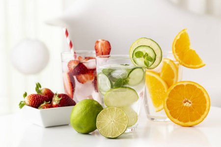 Foto de Vasos de agua infundida con lima fresca, pepino y hojas de menta, naranja y fresas. Enfoque selectivo en el primer vaso y la mitad de cal - Imagen libre de derechos