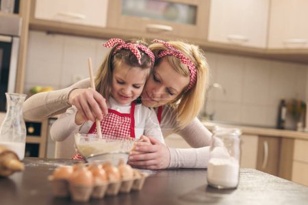 Photo for Beautiful little girl helping her mother in the kitchen to knead a pizza dough - Royalty Free Image