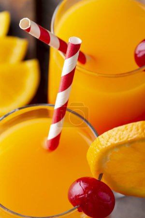 Photo for High angle view of two cold tequila sunrise cocktails with tequila, pomegranate juice and orange juice decorated with slices of orange and maraschino cherries. Selective focus on the straws - Royalty Free Image