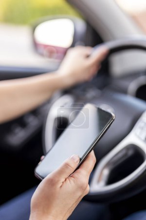 Téléchargez les photos : Détail des mains féminines tenant un volant et tapant un message texte sur un téléphone intelligent pendant la conduite d'une voiture - en image libre de droit