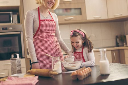 Téléchargez les photos : Pâte à pâte mère et fille ; fille semant de la farine à travers le tamis dans un bol à pétrir - en image libre de droit