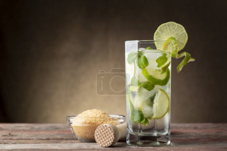 Téléchargez les photos : Cocktail de mojito avec beaucoup de glace, rhum blanc, jus de citron et tonique, décoré de tranches de lime et de feuilles de menthe sur une table en bois rustique - en image libre de droit