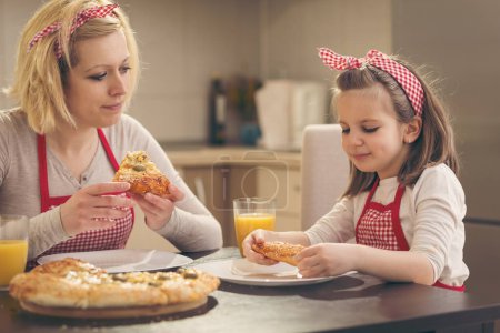 Foto de Madre e hija sentadas en la cocina, comiendo pizza y divirtiéndose. Concéntrate en la hija - Imagen libre de derechos