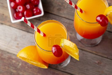 Foto de Vista de ángulo alto de dos cócteles de salida del sol de tequila fría con tequila, jugo de granada y jugo de naranja decorado con rodajas de cerezas de naranja y maraschino - Imagen libre de derechos