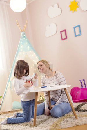 Foto de Madre e hija jugando en una sala de juegos, cortando papel, haciendo decoraciones - Imagen libre de derechos