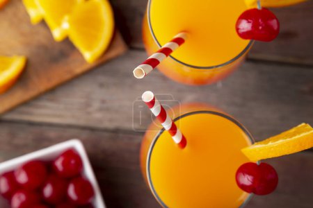 Photo for Table top shot of two cold tequila sunrise cocktails with tequila, pomegranate juice and orange juice decorated with slices of orange and maraschino cherries. Focus on the tips of the straws - Royalty Free Image