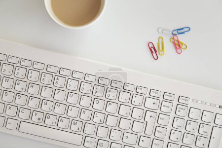 Téléchargez les photos : Plan de table d'un clavier d'ordinateur, trombones colorés et une tasse de café ; ambiance de travail à domicile - en image libre de droit