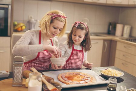 Téléchargez les photos : Mère et fille dans la cuisine faisant la pizza, mettre le salami sur la pâte à pizza - en image libre de droit