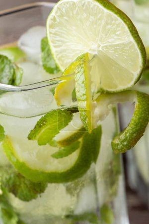 Téléchargez les photos : Détail du verre à cocktail mojito avec beaucoup de glace, rhum blanc, jus de citron et tonique, décoré de tranches de citron vert et de feuilles de menthe. Focus sélectif sur le bord du verre - en image libre de droit