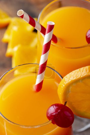 Photo for High angle view of two cold tequila sunrise cocktails with tequila, pomegranate juice and orange juice decorated with slices of orange and maraschino cherries. Focus on the tips of the straws - Royalty Free Image