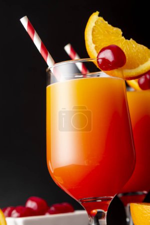 Photo for Two cold tequila sunrise cocktails with tequila, pomegranate juice and orange juice decorated with slices of orange and maraschino cherries. Focus on the cherry on the glass - Royalty Free Image