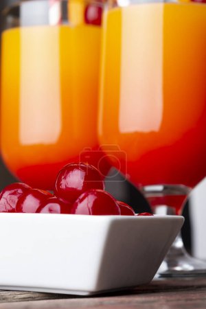 Photo for Detail of two cold tequila sunrise cocktails with tequila, pomegranate juice and orange juice decorated with slices of orange and maraschino cherries. Selective focus on the cherries - Royalty Free Image
