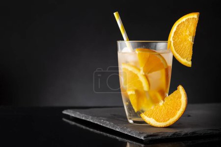 Téléchargez les photos : Verre d'eau fraîche infusée à froid avec des tranches d'orange, des glaçons et une paille à boire sur un plateau en pierre noire - en image libre de droit