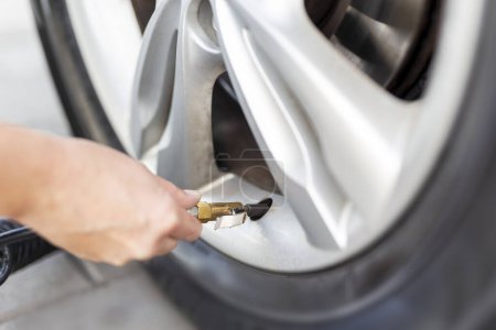 Foto de Detalle de la mano femenina que chequea la presión del neumático del coche usando el compresor en la gasolinera; mujer que infla un neumático del coche - Imagen libre de derechos