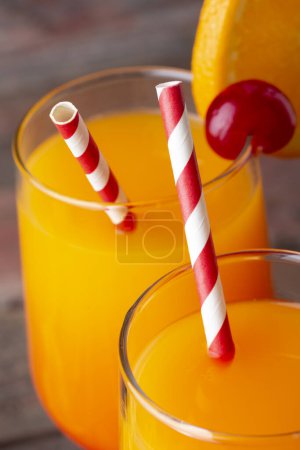 Photo for High angle view of two cold tequila sunrise cocktails with tequila, pomegranate juice and orange juice decorated with slices of orange and maraschino cherries. Focus on the tips of the straws - Royalty Free Image
