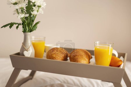 Téléchargez les photos : Plateau de petit déjeuner avec vase de fleurs, jus d'orange, croissants et café placés sur le lit. Focus sélectif sur les croissants - en image libre de droit