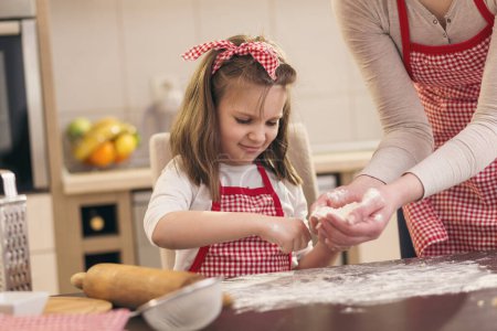 Foto de Niña rociando harina sobre la mesa de la cocina, ayudando a su madre a hornear una masa de pizza - Imagen libre de derechos
