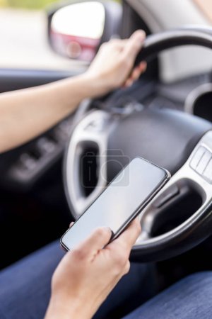 Foto de Detalle de las manos femeninas sosteniendo un volante y escribiendo un mensaje de texto en un teléfono inteligente mientras conduce un automóvil - Imagen libre de derechos