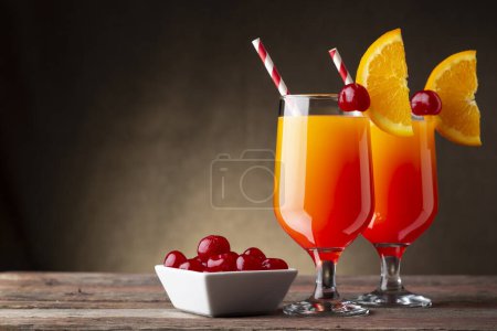Foto de Dos cócteles fríos de tequila al amanecer con tequila, zumo de granada y zumo de naranja decorados con rodajas de cerezas de naranja y maraschino - Imagen libre de derechos