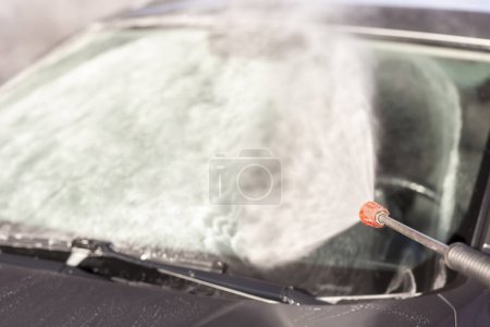 Téléchargez les photos : Détail du lavage d'un pare-brise de voiture avec de l'eau chaude haute pression et du détergent dans un lave-auto - en image libre de droit