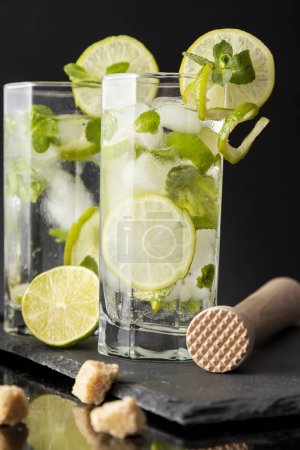 Foto de Copas de cóctel de mojito frío con ron blanco, zumo de limón y tónico decorado con rodajas de lima y hojas de menta - Imagen libre de derechos