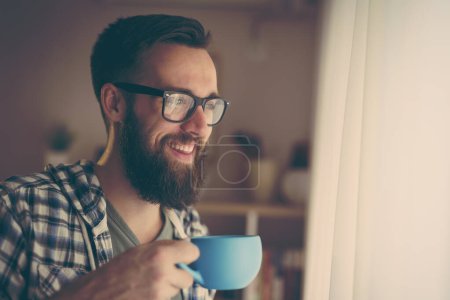 Foto de Hombre guapo de pie junto a una ventana, bebiendo café - Imagen libre de derechos