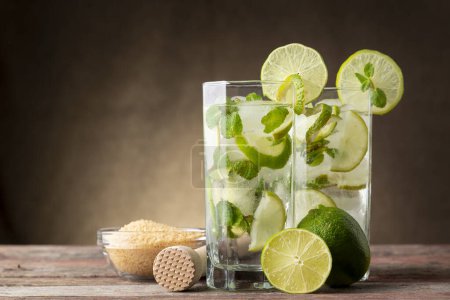 Photo for Two mojito cocktails with lots of ice, white rum, lemon juice and tonic, decorated with lime slices and mint leaves on a rustic wooden table - Royalty Free Image
