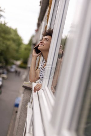 Foto de Retrato de una hermosa joven mirando por la ventana, conversando por teléfono y relajándose en casa - Imagen libre de derechos