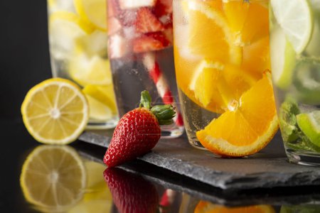Foto de Detalle de cuatro vasos de agua infundida con fresas frescas, lima, pepino y hojas de menta, limón y naranja. Concéntrate en la fresa - Imagen libre de derechos