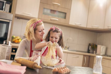 Foto de Hermosa niña amasando masa con su ayuda de las madres divirtiéndose en la cocina - Imagen libre de derechos