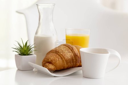 Foto de Desayuno en la mesa; cruasán fresco, vaso de jugo de naranja, botella de leche y una taza de café servido para el desayuno. Enfoque selectivo en el croissant - Imagen libre de derechos