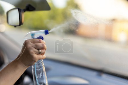 Téléchargez les photos : Détail du nettoyage à la main d'une femme d'un pare-brise de voiture tout en lavant la voiture avec spray nettoyant - en image libre de droit
