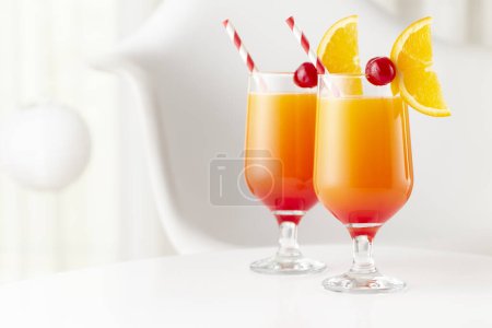 Photo for Two cold tequila sunrise cocktails with tequila, pomegranate juice and orange juice decorated with slices of orange and maraschino cherries. Focus on the cherry on the glass - Royalty Free Image