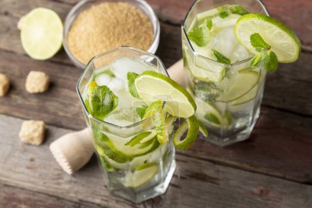 Photo for High angle view of two mojito cocktails with lots of ice, white rum, lemon juice and tonic, decorated with lime slices and mint leaves on a rustic wooden table - Royalty Free Image