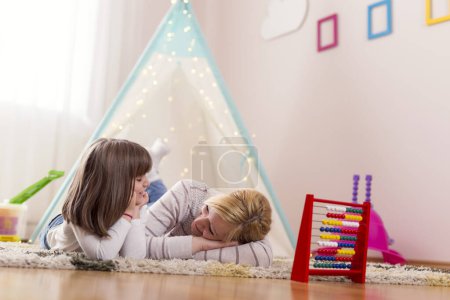 Foto de Madre e hija tumbadas en el suelo de una sala de juegos, hablando entre ellas y relajándose. Concéntrate en la madre - Imagen libre de derechos