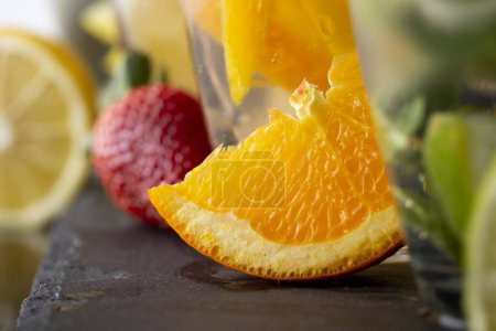 Foto de Detalle de cuatro vasos de agua infundida con fresas frescas, lima, pepino y hojas de menta, limón y naranja - Imagen libre de derechos