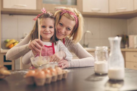Photo for Beautiful little girl helping her mother in the kitchen to knead a pizza dough - Royalty Free Image