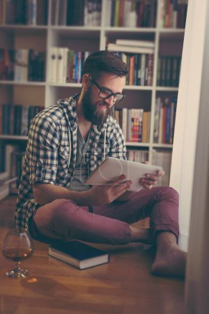 Photo for Young man enjoying his leisure time and relaxing while reading an ebook and having a drink - Royalty Free Image