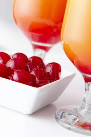 Photo for Detail of two cold tequila sunrise cocktails with tequila, pomegranate juice and orange juice decorated with slices of orange and maraschino cherries. Selective focus on the cherries - Royalty Free Image