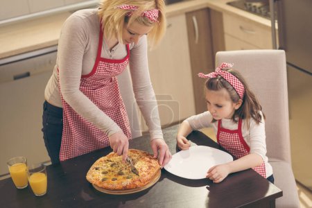 Foto de Madre e hija cortando pizza recién horneada lista para comer - Imagen libre de derechos