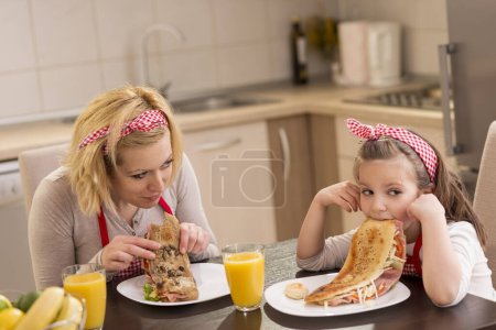 Foto de Madre e hija desayunando en la cocina; hija se niega a comer. Concéntrate en la madre - Imagen libre de derechos