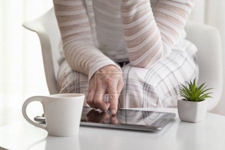 Téléchargez les photos : Détail des mains féminines utilisant un ordinateur tablette ; femme surfant sur le net sur un ordinateur tablette et buvant son café du matin. Focus sur l'index - en image libre de droit