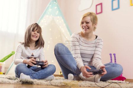 Foto de Madre e hija sentadas en el suelo en una sala de juegos, jugando videojuegos y divirtiéndose. Concéntrate en la madre - Imagen libre de derechos