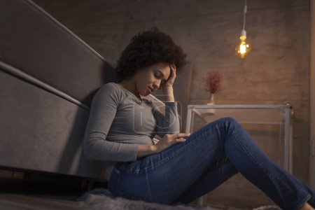 Photo for Beautiful young mixed race woman sitting on the floor by the bed with her eyes closed, tired after a long day, sad and stressed out - Royalty Free Image